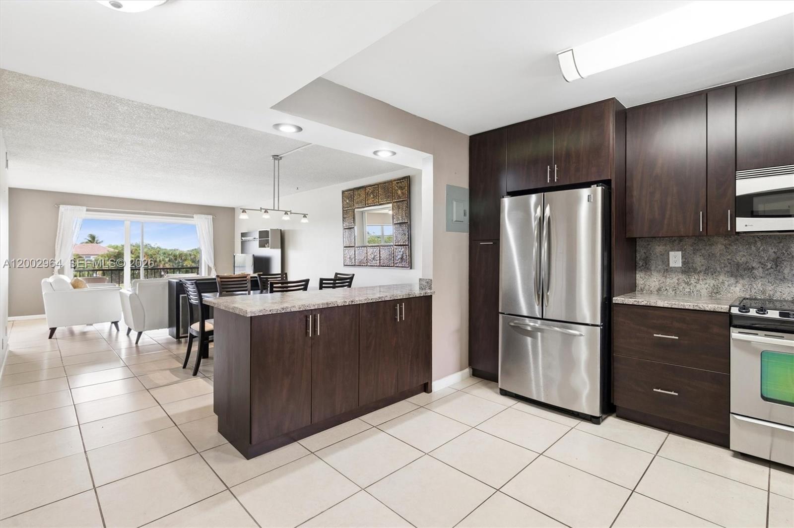 A kitchen with dark wood cabinets and stainless steel appliances opens to a dining area — PEMBROKE PINES, FL