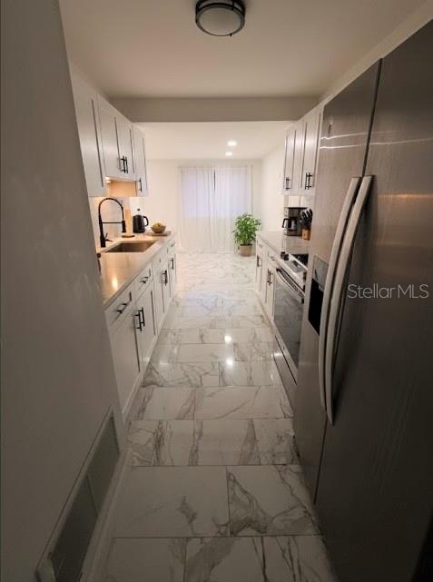 A galley kitchen features white cabinets, marble-patterned tile flooring, and stainless steel appliances — 7714 W POWHATAN, TAMPA, FL