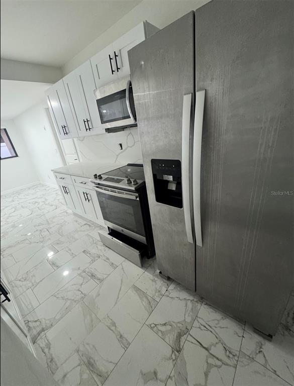 A kitchen features white cabinets, stainless steel appliances, and white marble-patterned tile flooring — 7714 W POWHATAN, TAMPA, FL