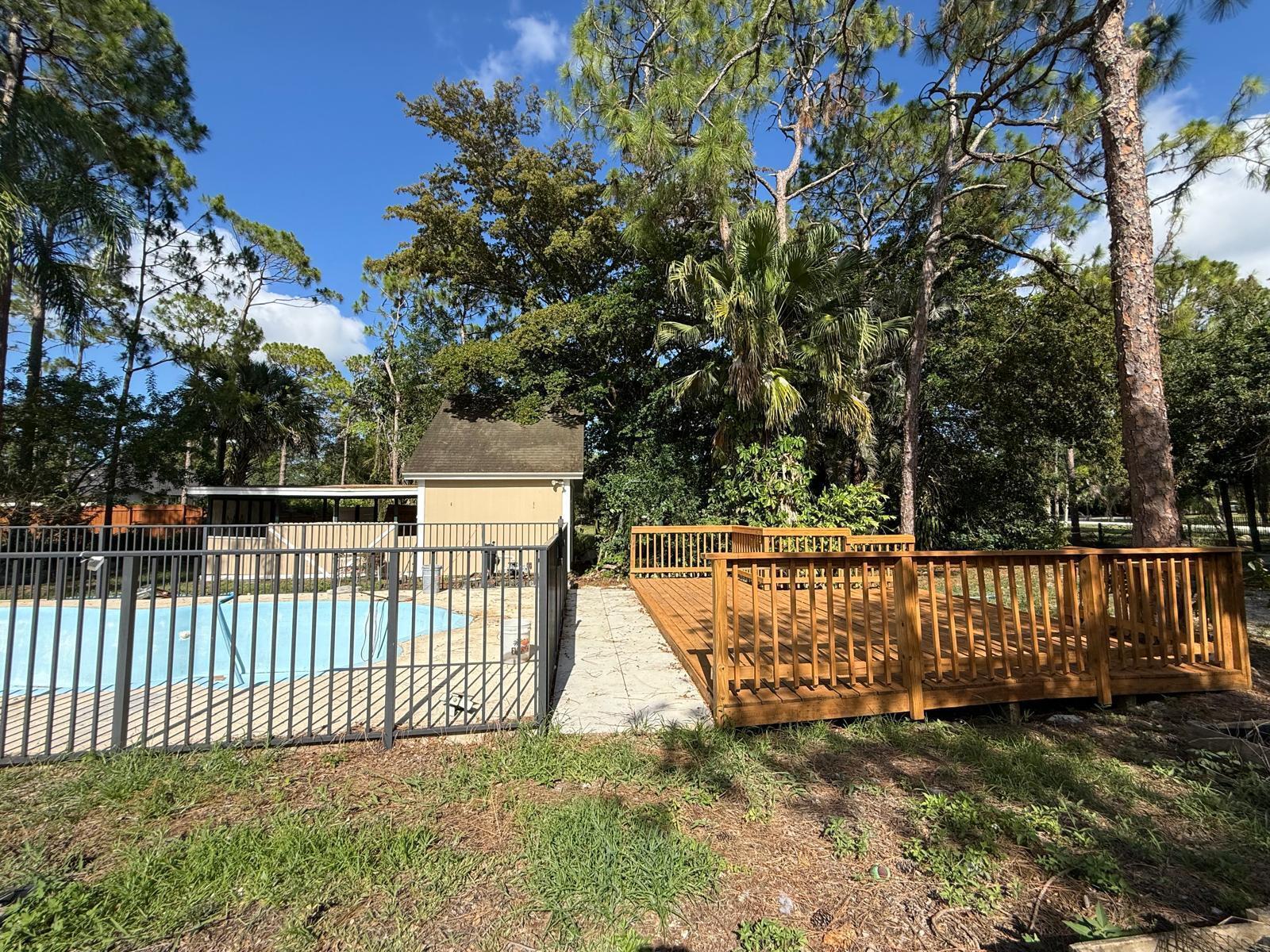 A backyard features a swimming pool with a metal fence next to a wooden deck — 17503 30th Lane N, Loxahatchee FL 33470, LOXAHATCHEE, FL