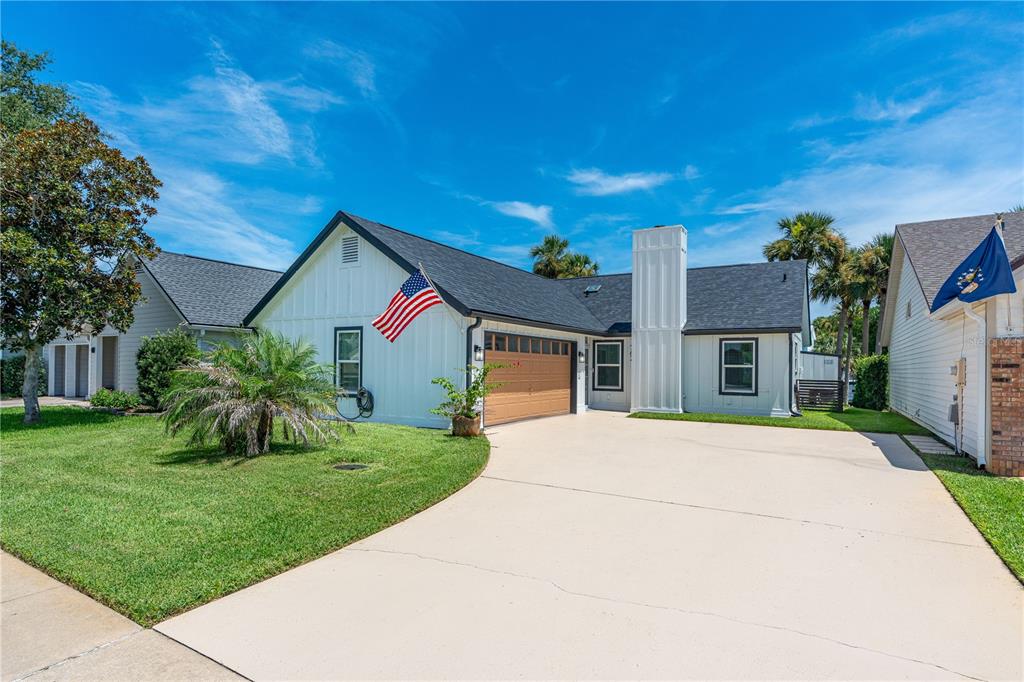 A white house with a dark roof, a wooden garage door, and an American flag — 762 PINE SHORES CIRCLE, NEW SMYRNA BEACH, FL