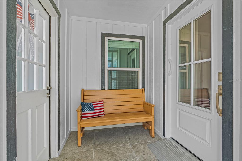 A wooden bench with an American flag pillow sits on a tiled porch between two doors — 762 PINE SHORES CIRCLE, NEW SMYRNA BEACH, FL