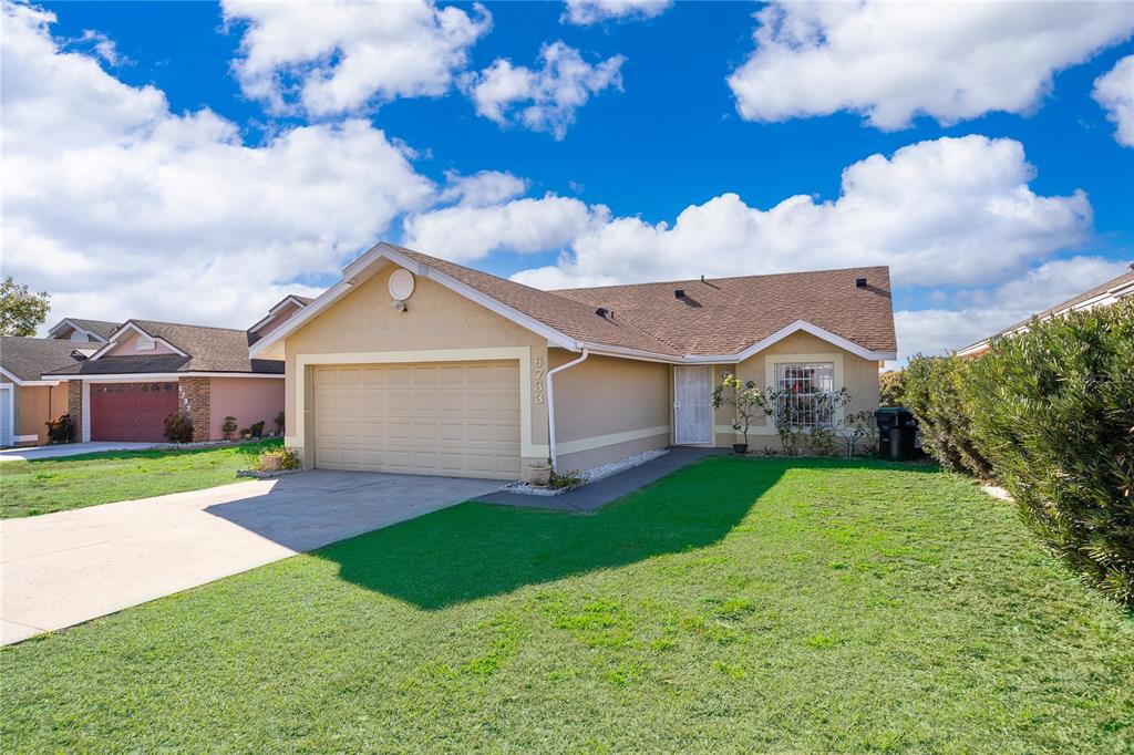 A single-story house with a tan stucco exterior, a two-car garage, and a front lawn — 6733 MERITMOOR CIRCLE, ORLANDO, FL