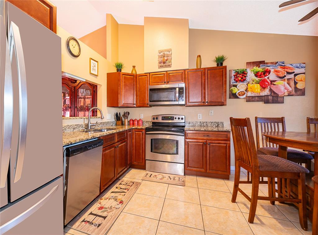 A kitchen with wooden cabinets, stainless steel appliances, granite countertops, and tile flooring — 6733 MERITMOOR CIRCLE, ORLANDO, FL