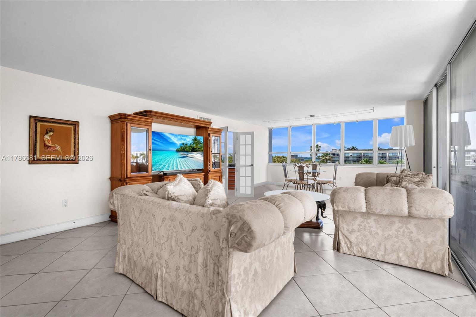 A living room features beige patterned sofas, a large wooden entertainment center, and floor-to-ceiling windows — 11 Island Ave # 512, Miami Beach FL 33139, MIAMI BEACH, FL