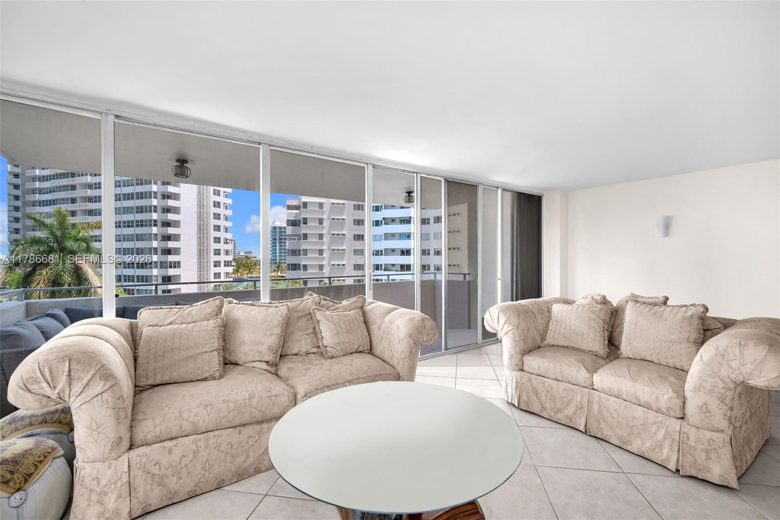 A living room features two beige patterned sofas, a round coffee table, and floor-to-ceiling windows — 11 Island Ave # 512, Miami Beach FL 33139, MIAMI BEACH, FL