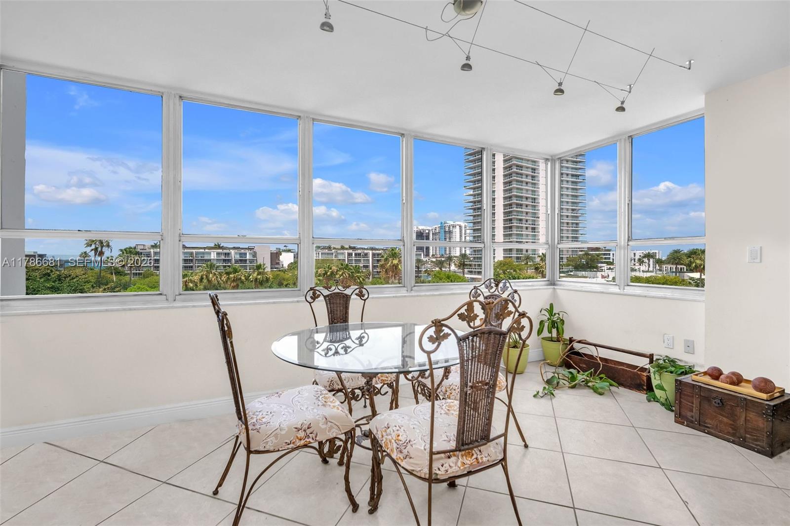 A sunroom features a glass-topped dining set, tile flooring, and floor-to-ceiling windows with city views — 11 Island Ave # 512, Miami Beach FL 33139, MIAMI BEACH, FL
