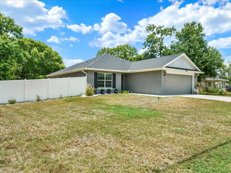 A gray single-story house with a two-car garage and a white vinyl fence — 15648 SE 92ND AVENUE, SUMMERFIELD, FL