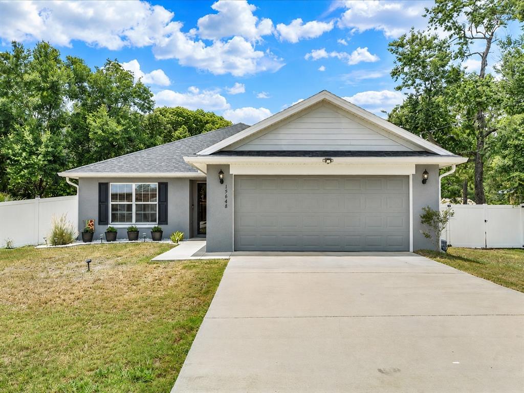 A single-story gray house with a two-car garage, white trim, and a concrete driveway — 15648 SE 92ND AVENUE, SUMMERFIELD, FL