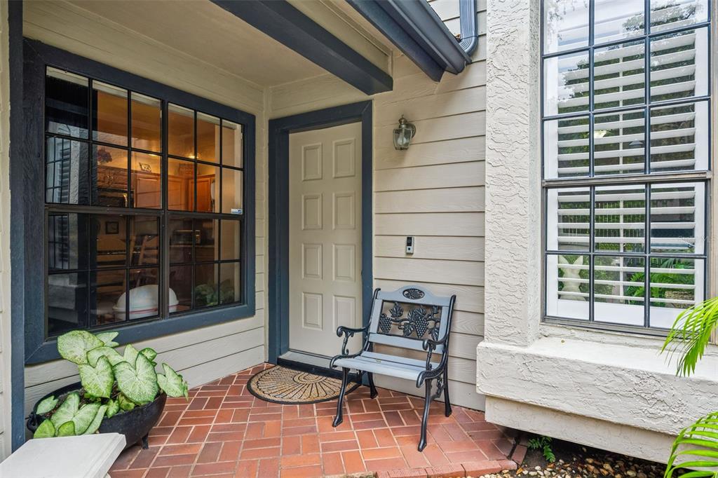 A brick-floored entryway features a light-colored door, a metal bench, and large grid-pattern windows — 1123 BENT BIRCH COURT, ALTAMONTE SPRINGS, FL