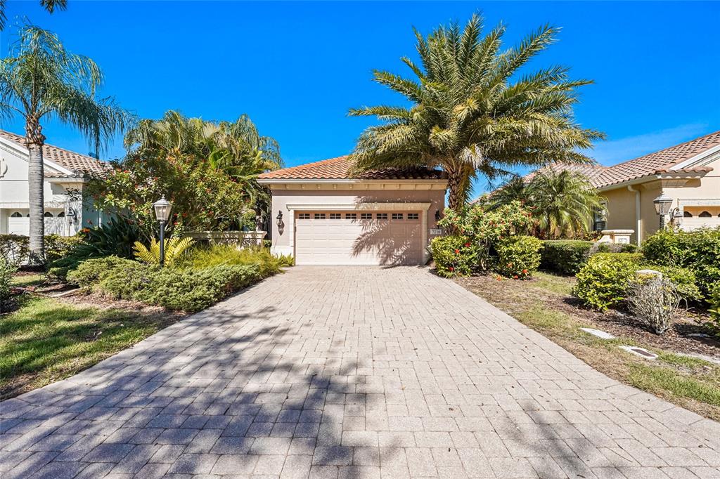 A paved driveway leads to the garage of a single-story house with palm trees — 7216 PRESIDIO GLEN, LAKEWOOD RANCH, FL