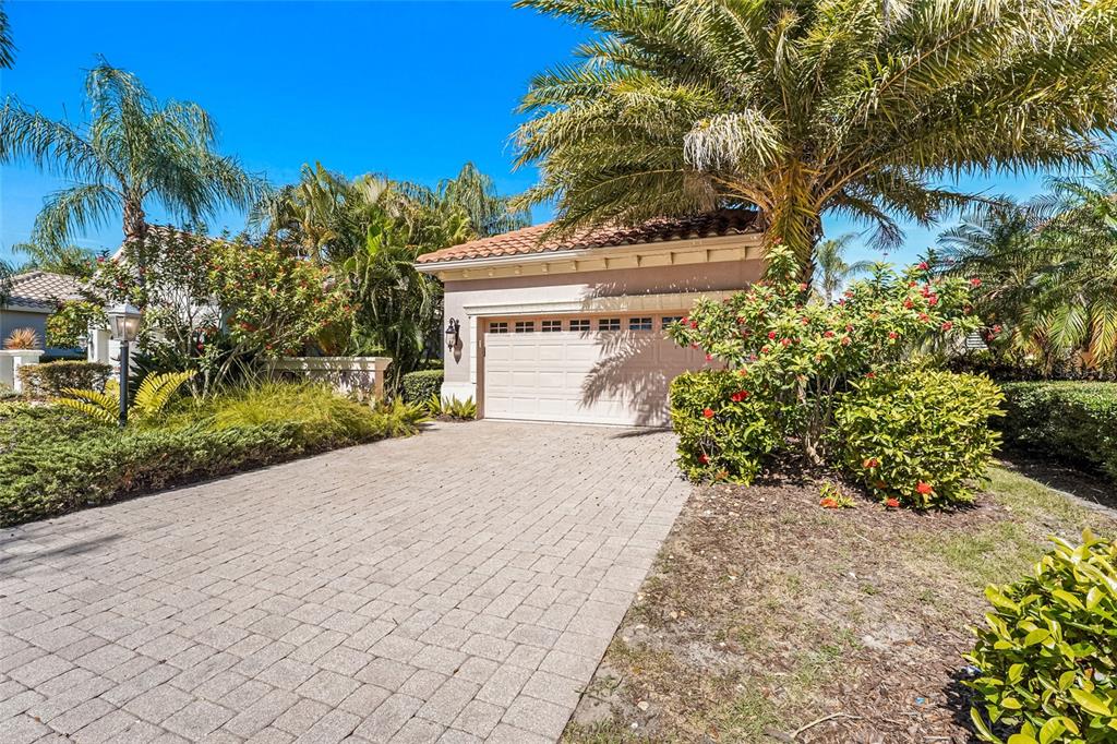 A paved driveway leads to a one-car garage of a house surrounded by palm trees — 7216 PRESIDIO GLEN, LAKEWOOD RANCH, FL