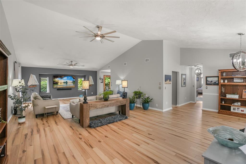 A spacious living room features light wood flooring, vaulted ceilings, and a gray accent wall — 112 PEACHTREE CIRCLE, DAYTONA BEACH, FL