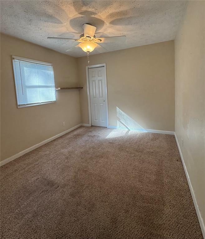 An empty bedroom features beige walls, tan carpeting, a ceiling fan, and a single door — 22368 PANORAMA STREET, BROOKSVILLE, FL