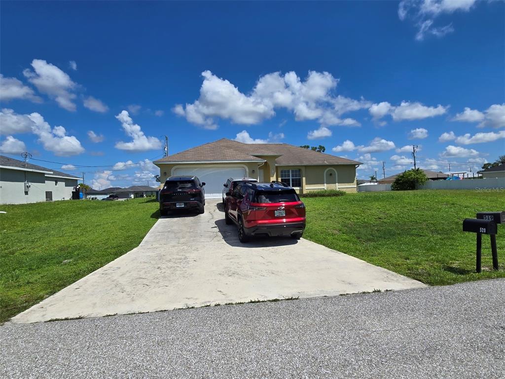 A single-story house with a concrete driveway and two parked cars sits under a blue sky — 519 NW 26TH STREET, CAPE CORAL, FL