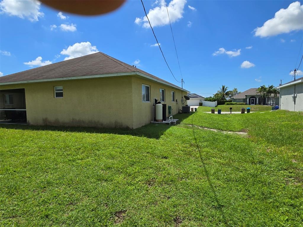 The exterior side view of a yellow house features a lawn and utility equipment — 519 NW 26TH STREET, CAPE CORAL, FL
