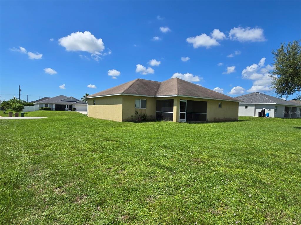 The exterior rear view of a single-story house features a screened-in porch and a large lawn — 519 NW 26TH STREET, CAPE CORAL, FL