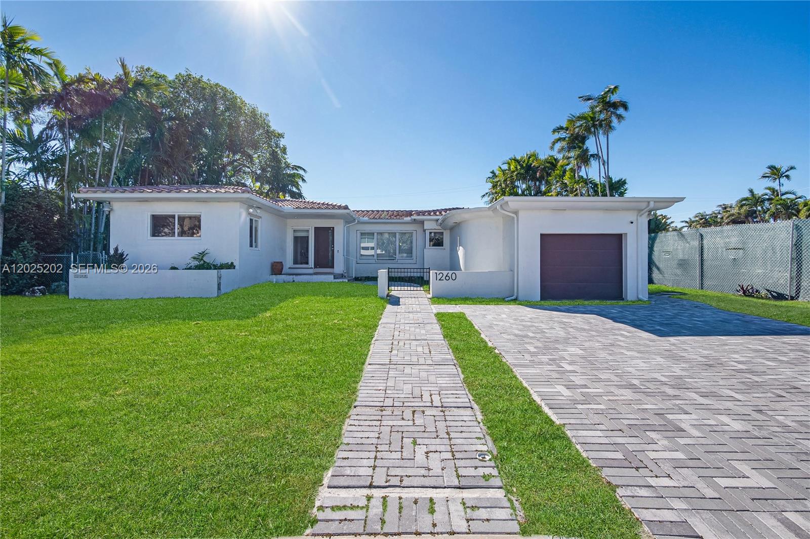 A single-story white house features a tiled roof, a paved driveway, and a front walkway — 1260 99th St, Bay Harbor Islands FL 33154, BAY HARBOR ISLANDS, FL