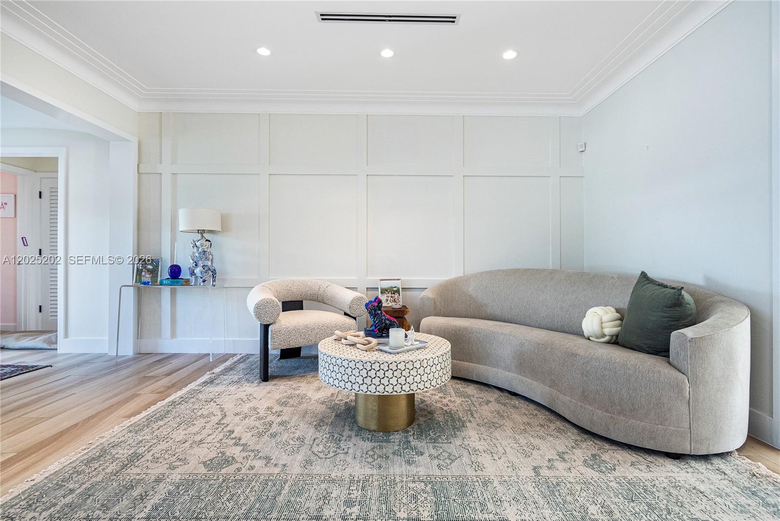 A living room features a curved sofa, a patterned coffee table, and paneled walls — 1260 99th St, Bay Harbor Islands FL 33154, BAY HARBOR ISLANDS, FL