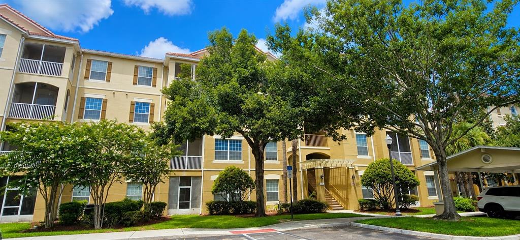 A multi-story apartment building with beige stucco walls and a covered parking area — 3326 ROBERT TRENT JONES DRIVE UNIT 209, ORLANDO, FL