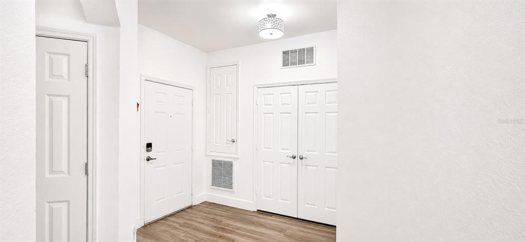 An entryway features white walls, wood-look flooring, a front door, and several closet doors — 3326 ROBERT TRENT JONES DRIVE UNIT 209, ORLANDO, FL