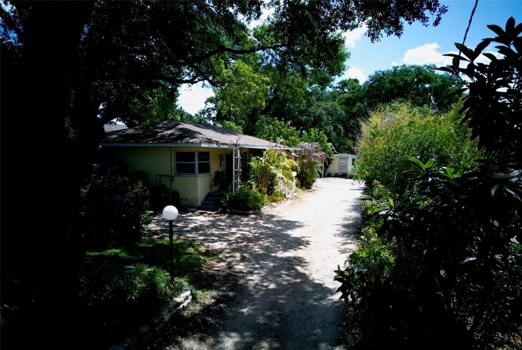 A yellow house with a gravel driveway sits among mature trees and lush landscaping — 2119 S FERN CREEK AVENUE, ORLANDO, FL