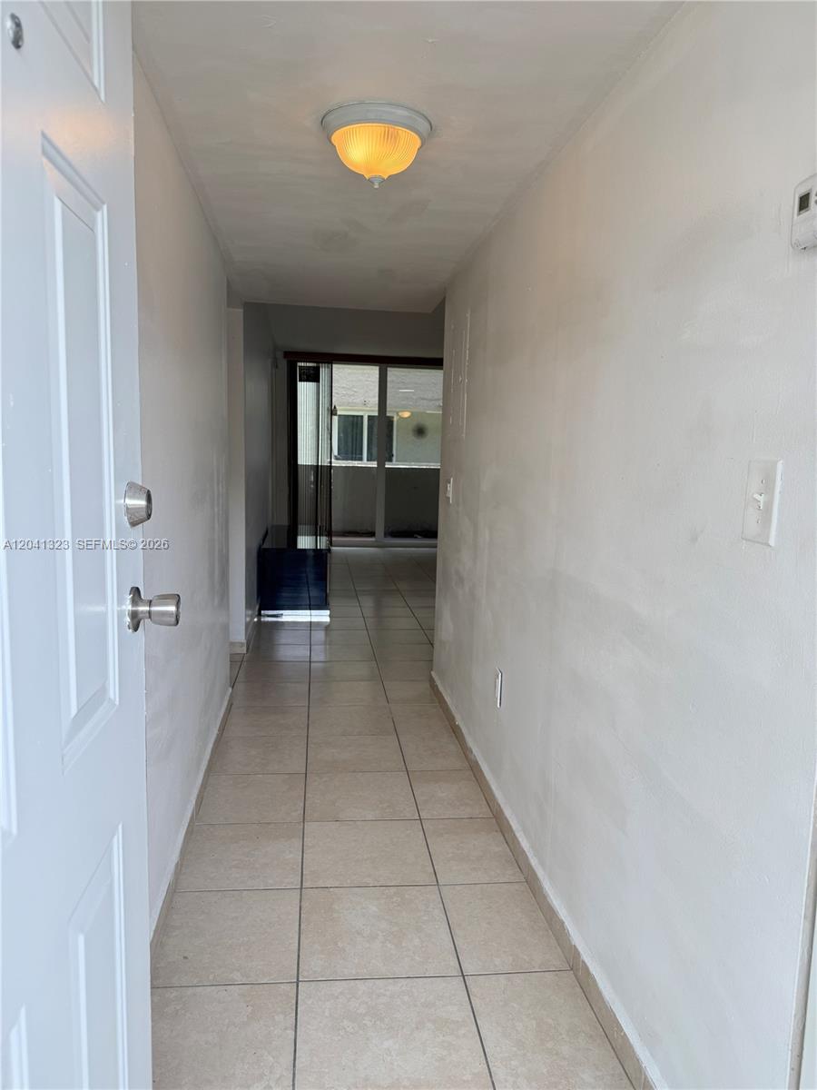 A tiled hallway leads from an open door toward a balcony with sliding glass doors — 10090 NW 80th Ct # 1241, Hialeah Gardens FL 33016, HIALEAH GARDENS, FL
