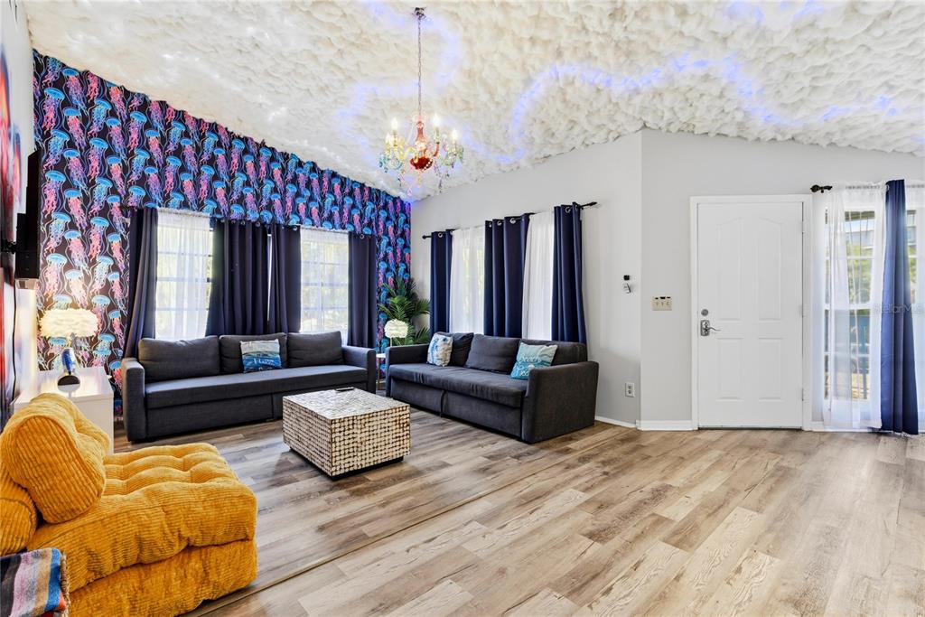 A living room features a jellyfish-patterned accent wall, a cloud-textured ceiling, and two gray sofas — 527 BEACH ROAD, SARASOTA, FL