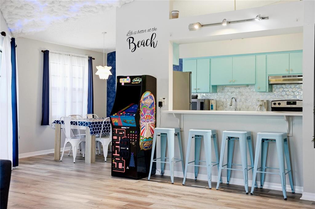 An open-concept kitchen and dining area features light blue cabinets, bar stools, and an arcade game — 527 BEACH ROAD, SARASOTA, FL