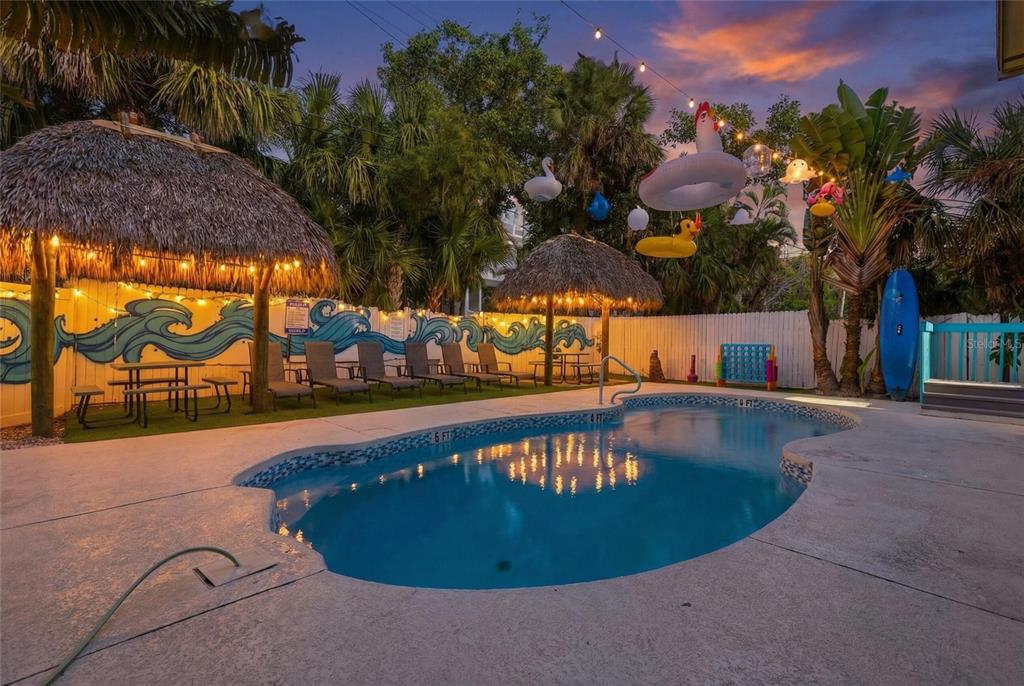 A backyard swimming pool features two tiki huts, lounge chairs, and hanging pool floats — 527 BEACH ROAD, SARASOTA, FL