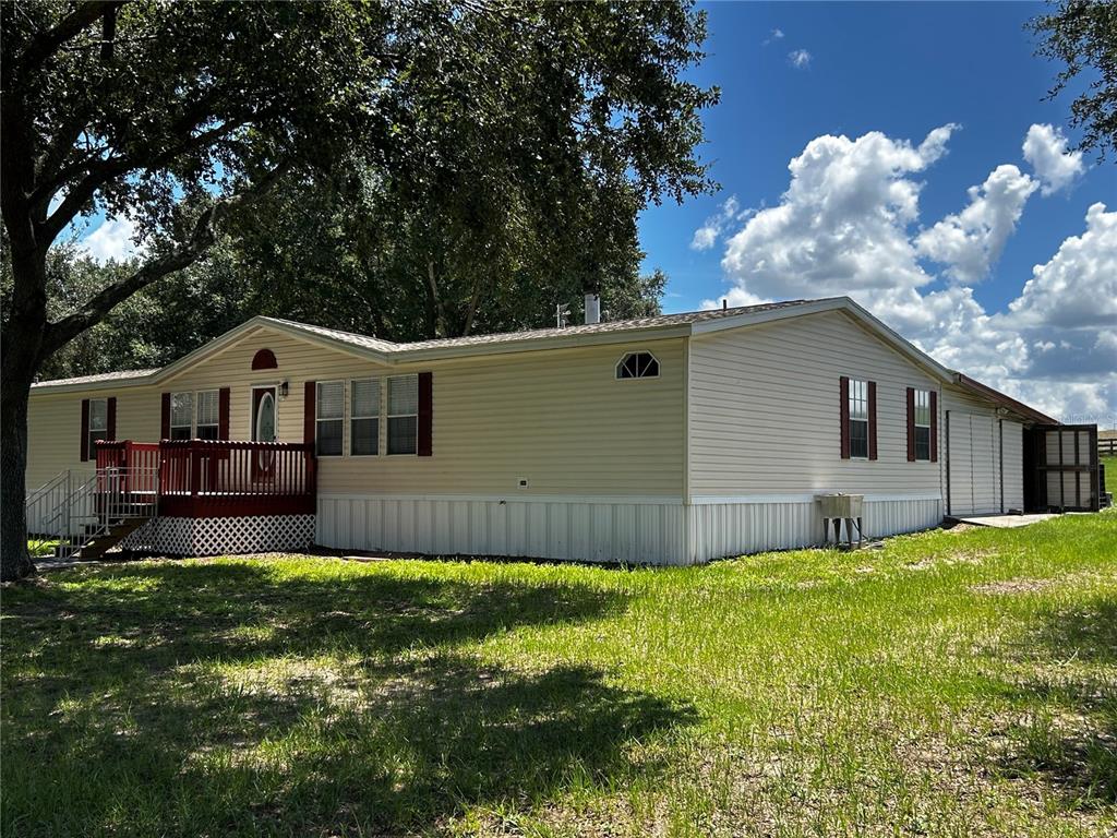 A light-colored manufactured home with a red wooden deck sits on a grassy lot — 8535 23RD STREET, ZEPHYRHILLS, FL