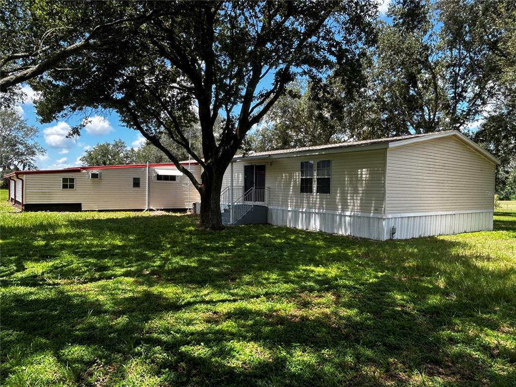 A mobile home with light-colored siding sits on a grassy lot under a large tree — 8535 23RD STREET, ZEPHYRHILLS, FL
