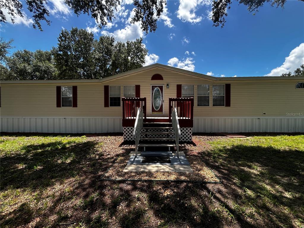 A single-story manufactured home with light siding, red shutters, and a front wooden porch — 8535 23RD STREET, ZEPHYRHILLS, FL