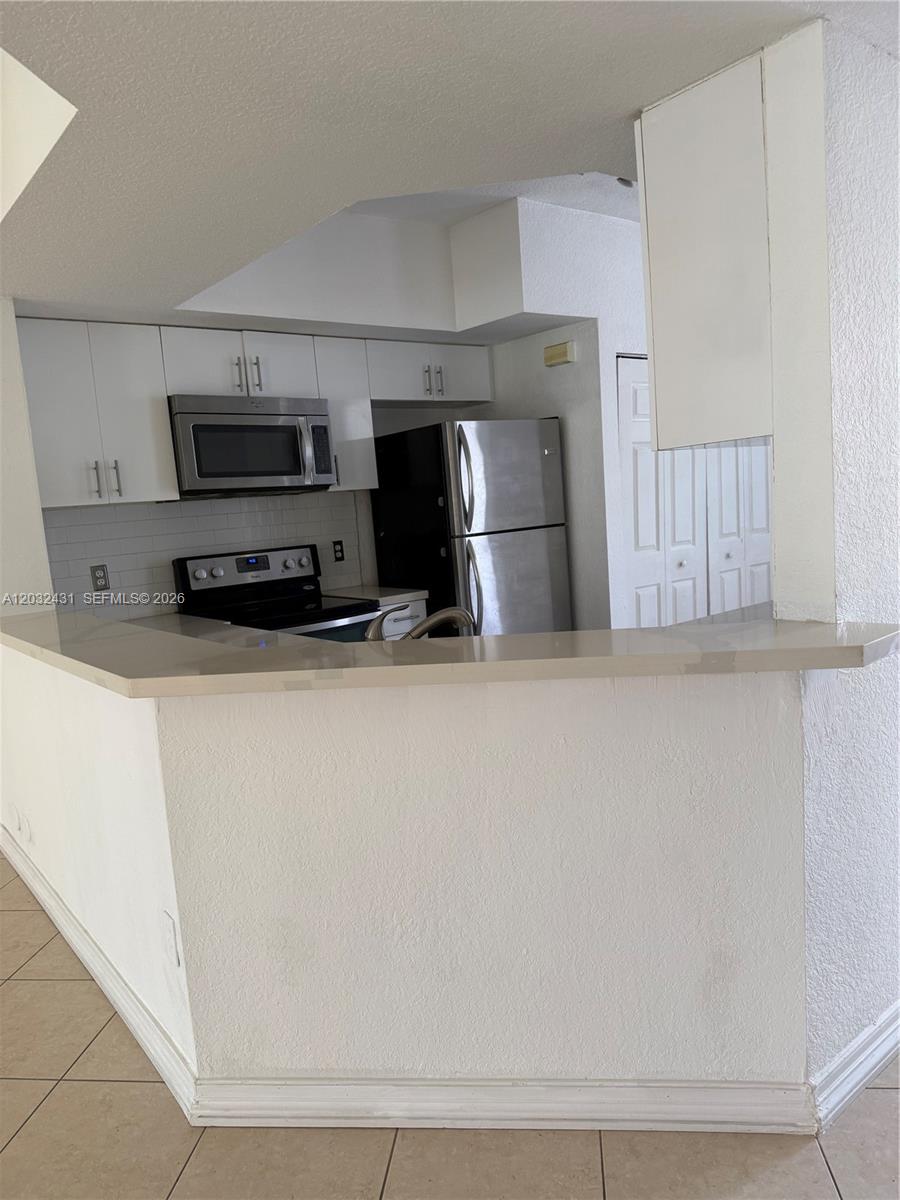 A kitchen features white cabinets, stainless steel appliances, and a breakfast bar with stone countertops — 715 SW 148th Ave # 611, Sunrise FL 33325, SUNRISE, FL