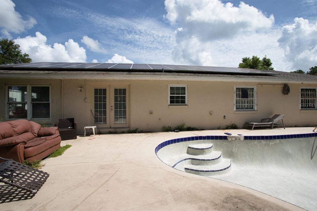 A backyard features a swimming pool, a patio with a sofa, and solar panels on the roof — 7408 NAVEL TREE COURT, ORLANDO, FL