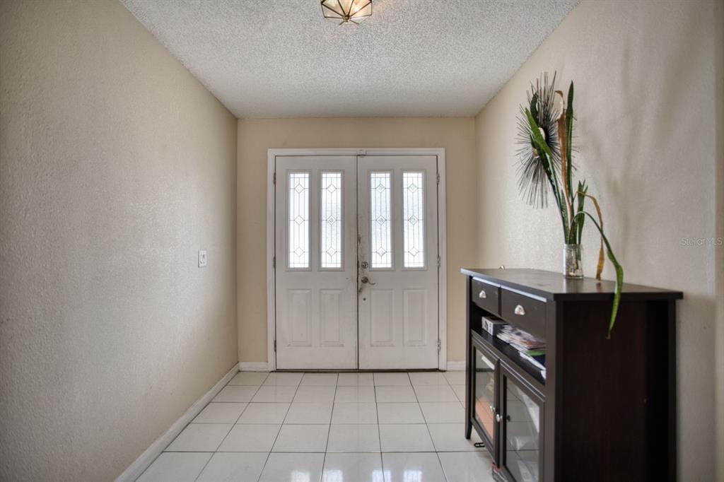 A white-tiled entryway features double front doors with glass panels and a dark wood cabinet — 7408 NAVEL TREE COURT, ORLANDO, FL