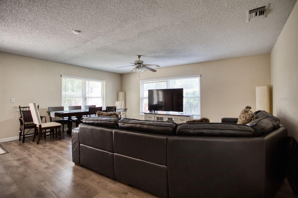A living room with a dark leather sectional, dining area, and wood-look flooring — 7408 NAVEL TREE COURT, ORLANDO, FL