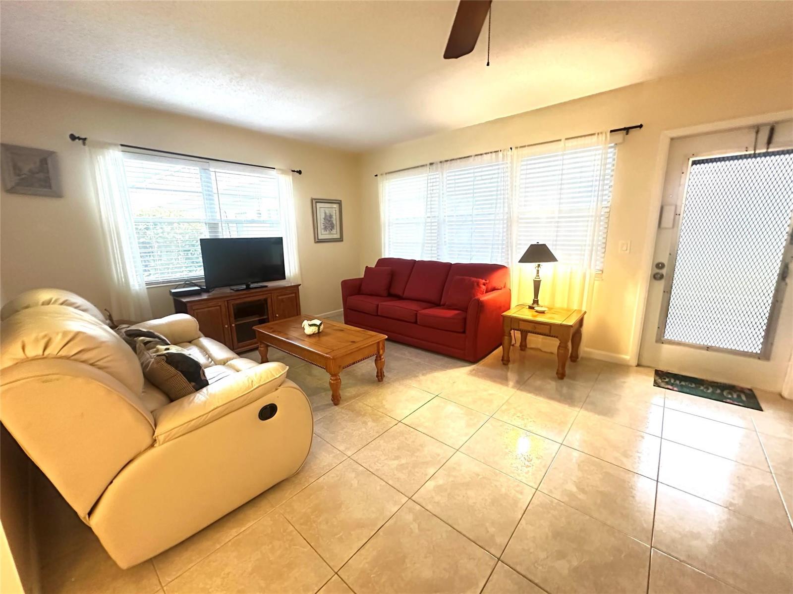 A living room features tile flooring, a red sofa, a beige recliner, and wooden furniture — 489 Tilford W # 489, Deerfield Beach FL 33442, DEERFIELD BEACH, FL