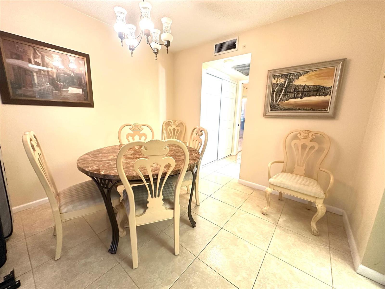 A dining area features a round marble-top table, four chairs, a chandelier, and tiled flooring — 489 Tilford W # 489, Deerfield Beach FL 33442, DEERFIELD BEACH, FL