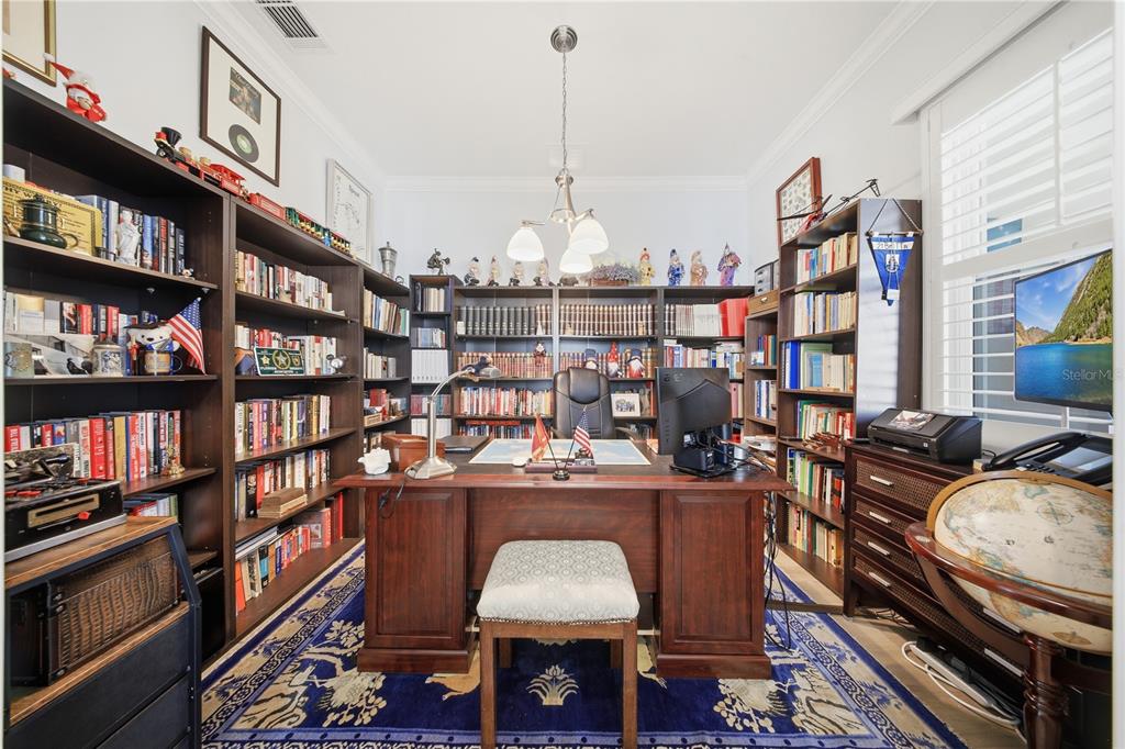 A home office features dark wood bookshelves, a central desk, and a blue patterned rug — 1999 KEY BAY TRAIL, KISSIMMEE, FL