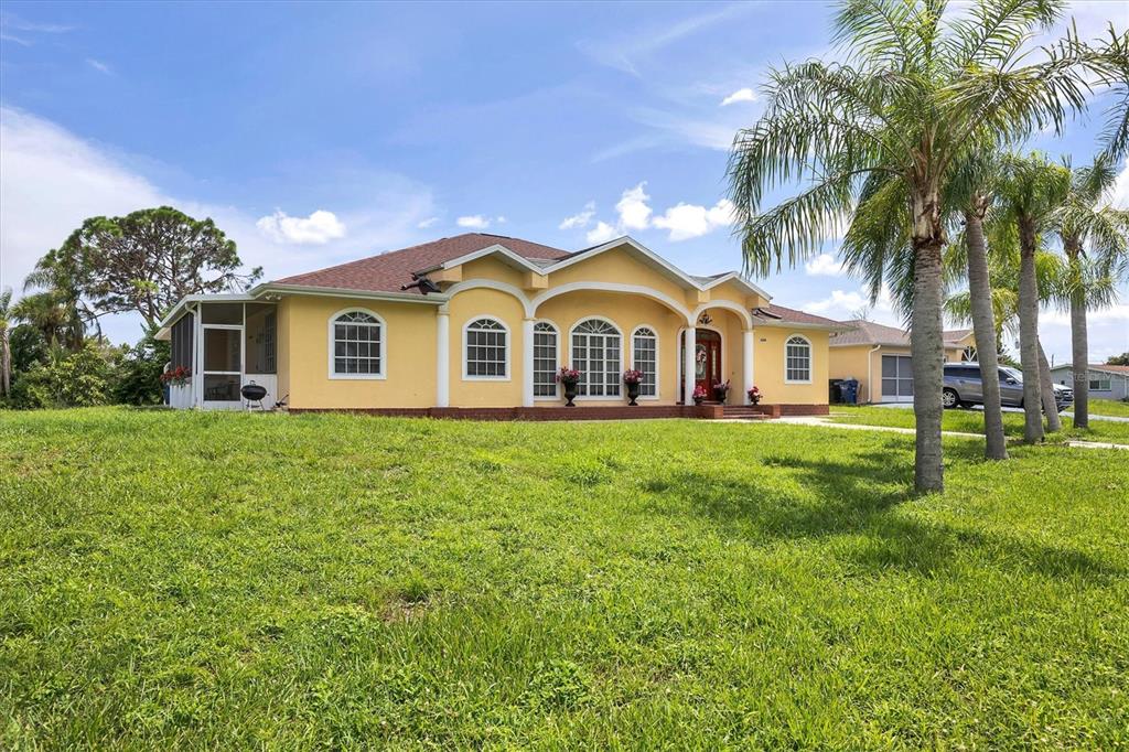A yellow single-story house with arched windows and a screened porch sits on a grassy lot — 12209 COTORRO AVENUE, NORTH PORT, FL