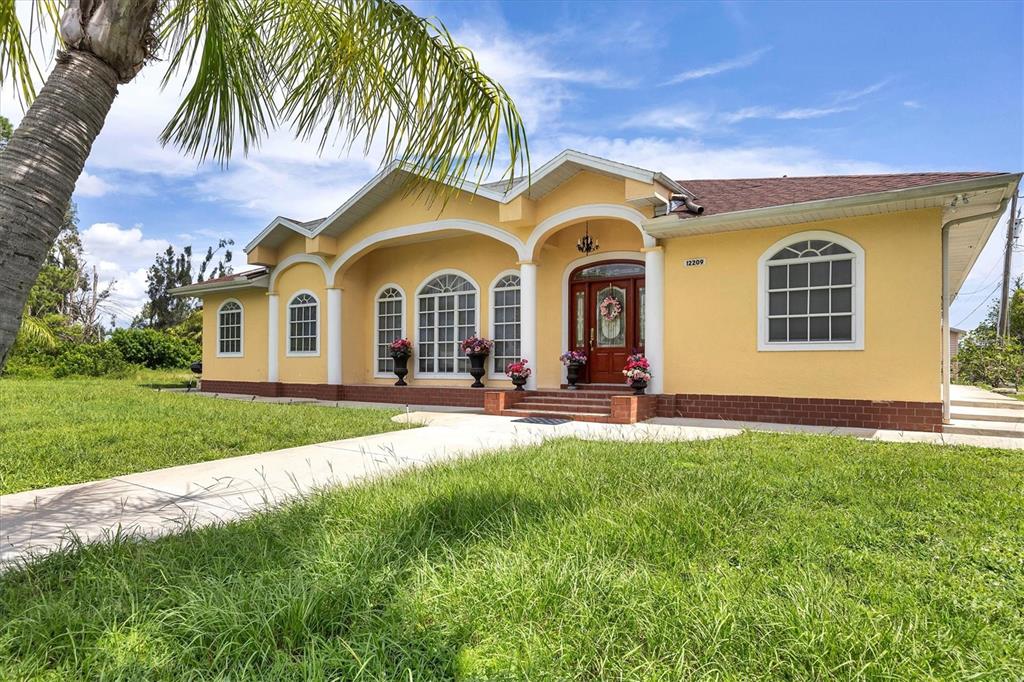 A yellow single-story house with a brick foundation, arched entryway, and a palm tree — 12209 COTORRO AVENUE, NORTH PORT, FL