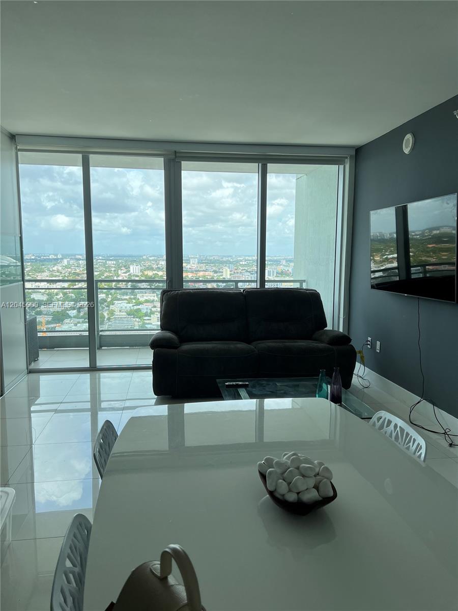 A living room with a dark sofa, glass coffee table, and floor-to-ceiling windows overlooking a city — 92 SW 3rd St # 3508, Miami FL 33130, MIAMI, FL