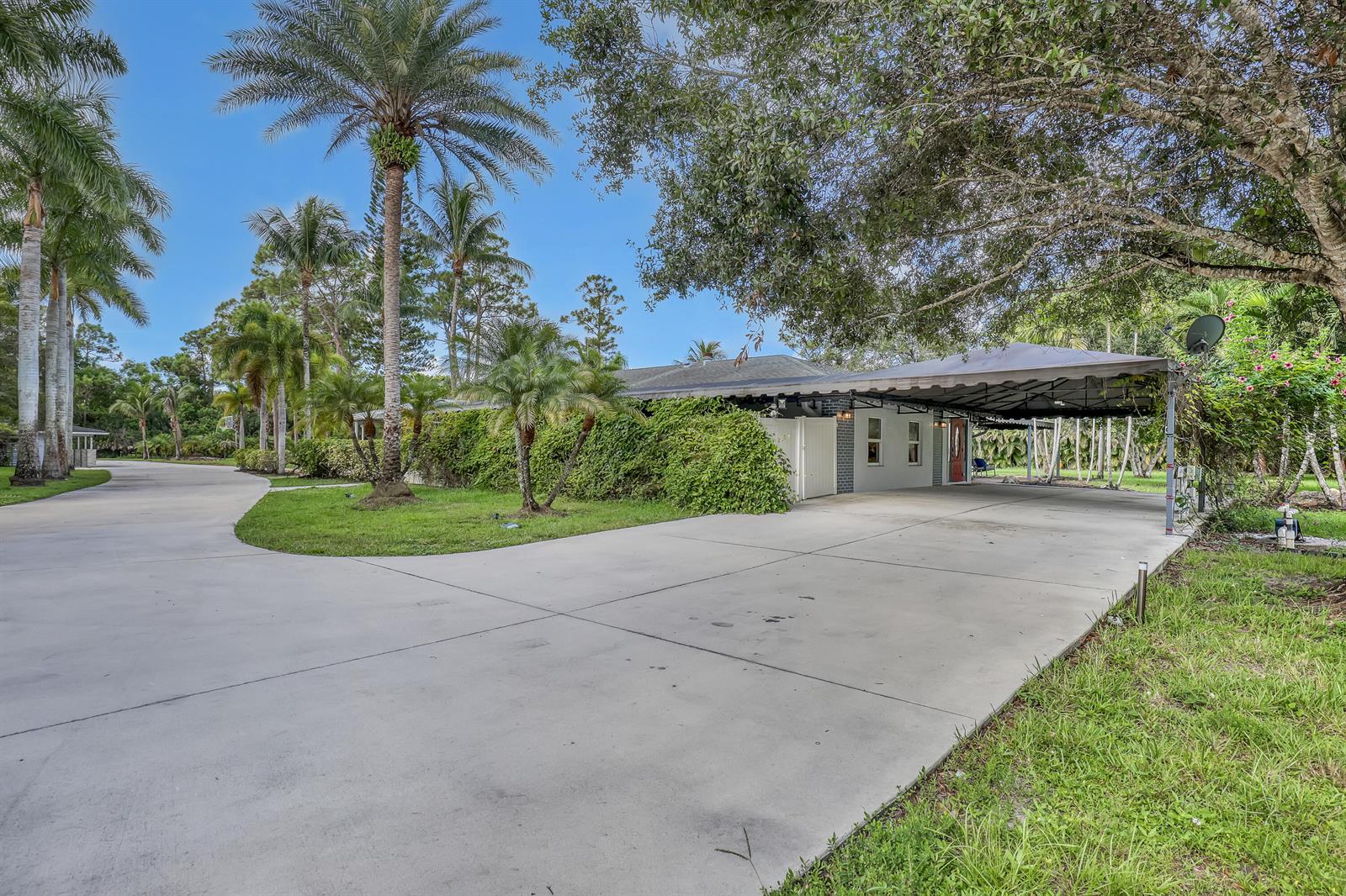 A single-story house with a large concrete driveway and a covered carport under mature trees — 10780 Anderson Lane, Wellington FL 33449, WELLINGTON, FL