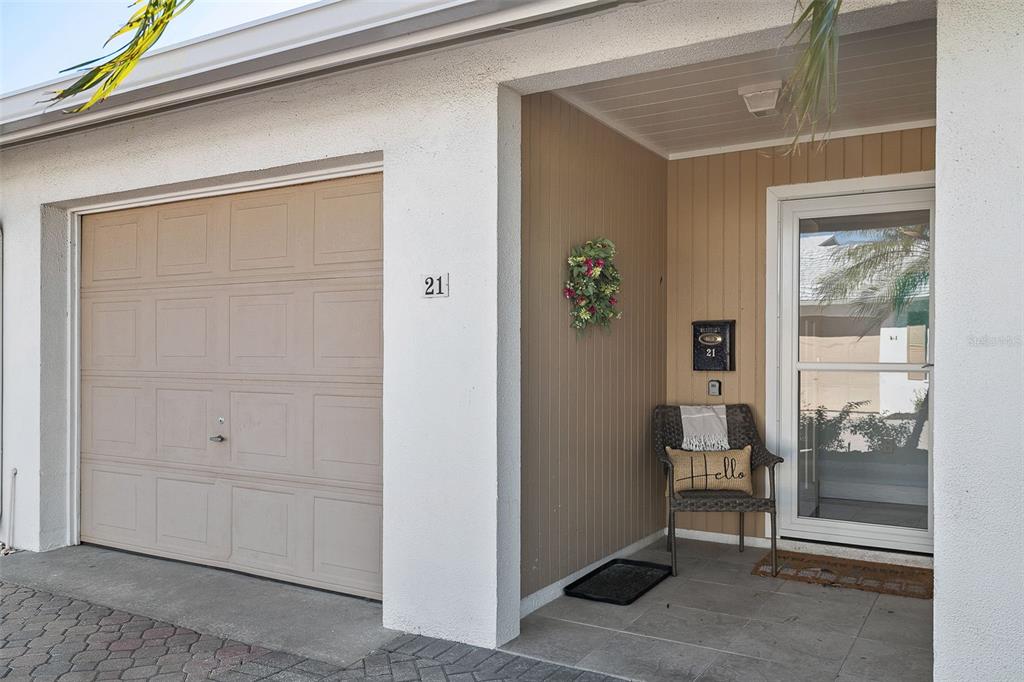 A beige garage door and a covered entryway with a chair and front door — 6300 MIDNIGHT PASS ROAD UNIT 21, SARASOTA, FL