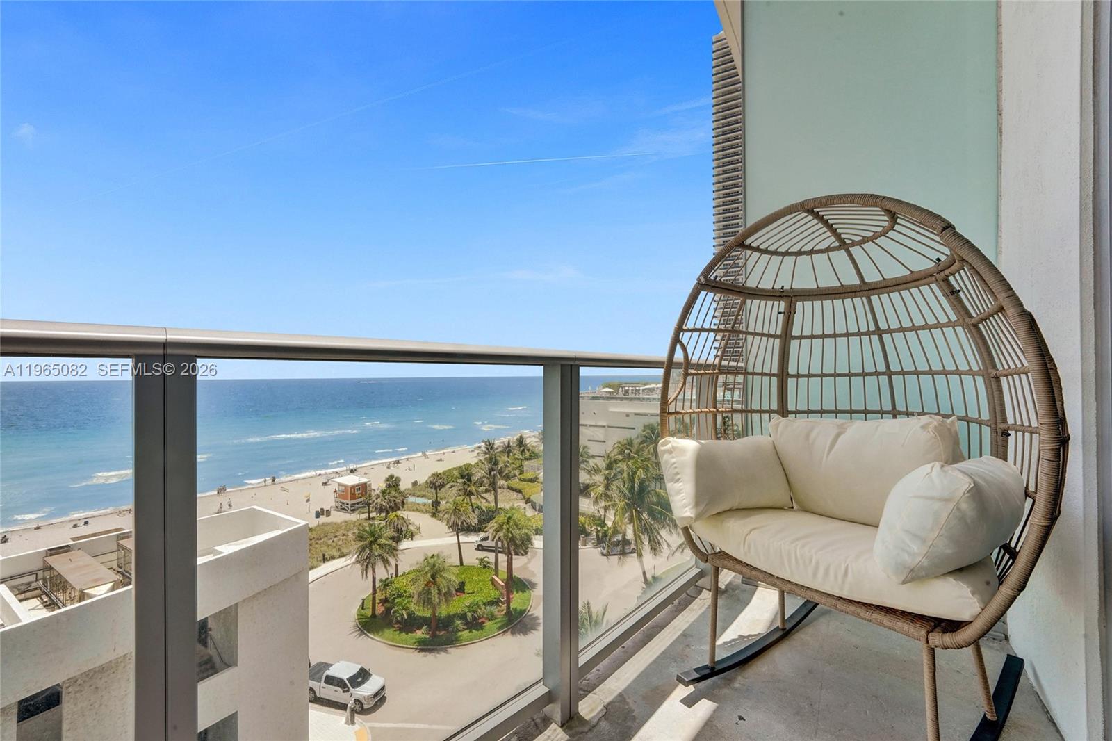 A balcony with a wicker egg chair overlooks a beach, palm trees, and the ocean — 4111 S Ocean Dr # 603, Hollywood FL 33019, HOLLYWOOD, FL