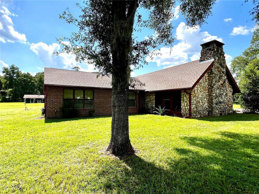 A brick and stone house with a large chimney sits on a grassy lawn — 7 MEADOW WOOD DRIVE, OCALA, FL