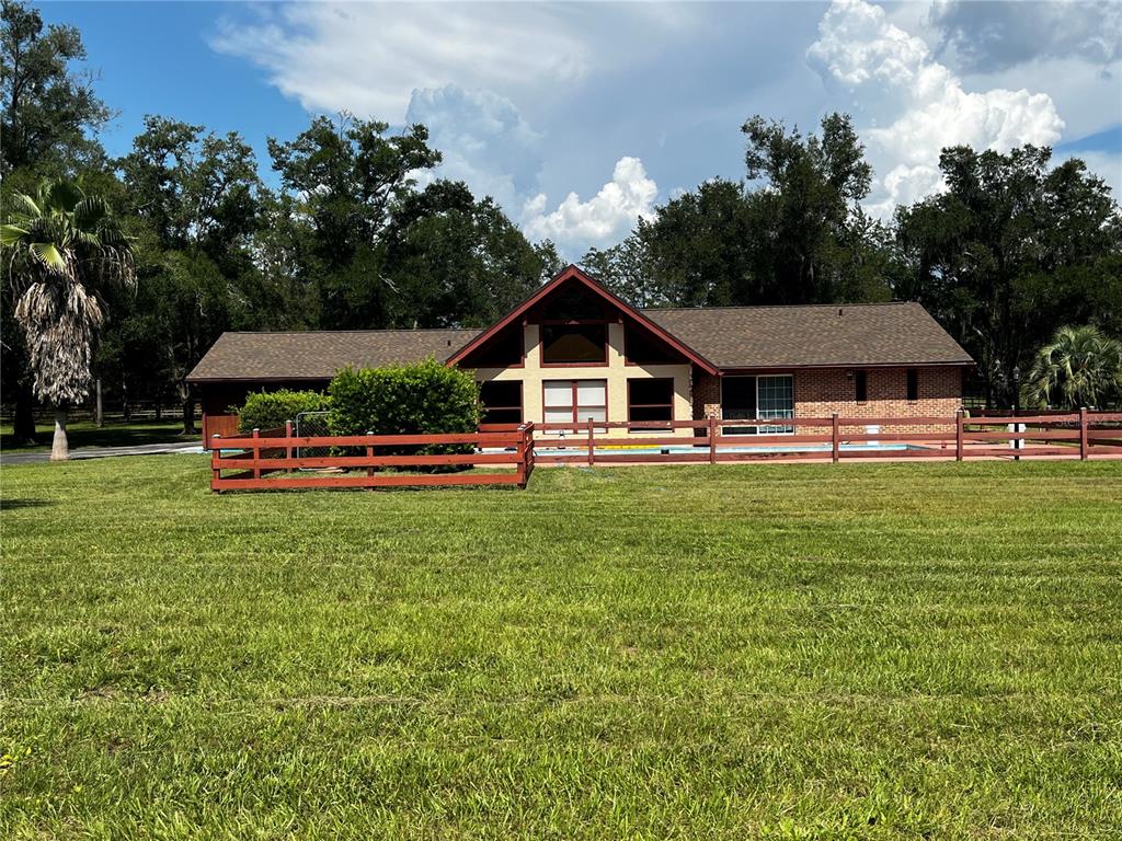 A single-story brick house with a prominent A-frame gable and a fenced-in swimming pool — 7 MEADOW WOOD DRIVE, OCALA, FL