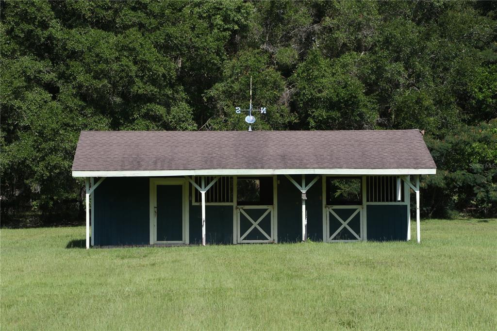 A blue wooden horse stable with a shingled roof sits in a grassy field — 7 MEADOW WOOD DRIVE, OCALA, FL