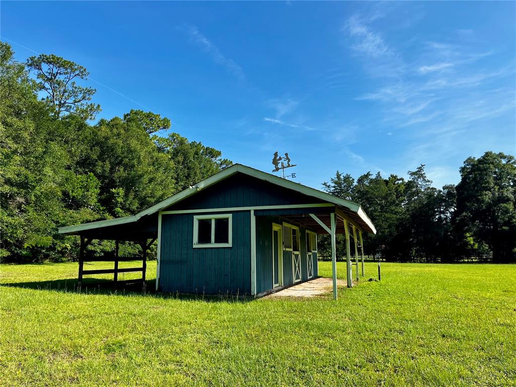 A blue barn with a metal roof and a covered porch sits in a grassy field — 7 MEADOW WOOD DRIVE, OCALA, FL